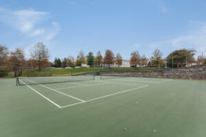 Exterior Acclaim at Ashburn tennis courts, tennis hard courts, autumn trees in the background, white buildings in the distance, photo taken on a sunny day.