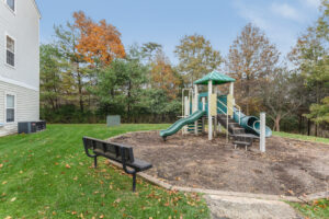Exterior Acclaim at Ashburn playground, soft landing ground, bench facing playground, autumn trees in the background, photo taken on a sunny day.