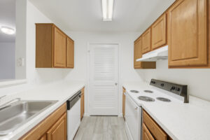Interior Unit Kitchen, Light brown cabinets, white appliances, stainless steel sink, wood floors, stone countertops.