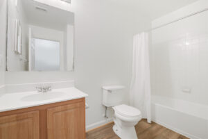 Interior Unit Bathroom, wood floors, large vanity mirror, light brown cabinetry, bathtub/shower, white countertop.