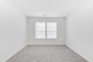 Interior Unit Bedroom, white walls, two windows, neutral toned carpeting.
