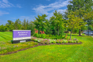 Exterior Acclaim at Ashburn Front Signage, meticulous landscaping, lush foliage, photo taken on a sunny day.